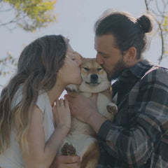 Couple kissing beside a tree holding a puppy